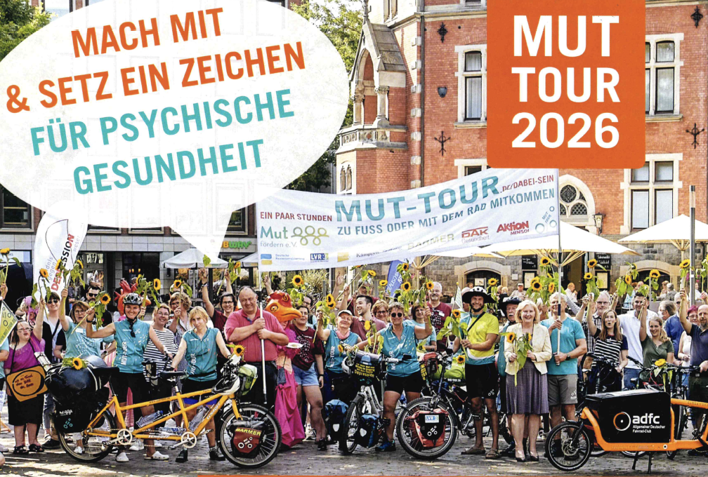 MUT_Tour Viele Personen unterschiedlichen Alters stehen mit Fahrrädern als Gruppe zusammen und halten ein Transparent mit der Aufschrift MUT-Tour hoch.